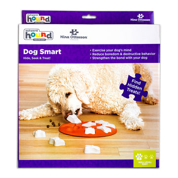 Outward Hound Nina Ottosson Dog Smart Level 1 puzzle toy packaging showing a fluffy white dog nosing the orange puzzle board to find hidden treats