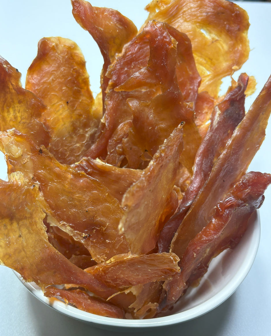 GoPetPlace Australian chicken breast jerky strips piled in a white bowl, showing the dried, golden-amber texture of the treat