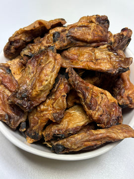 A white bowl piled high with dried chicken drumettes and wingettes dog treats