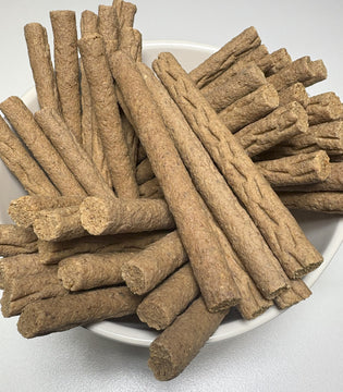 A white plate piled with GoPetPlace chicken mini sticks — soft, chewy, tan-coloured dog treats approximately 12.5cm long