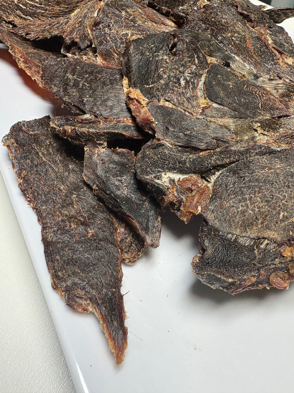 Close-up of dried kangaroo jerky pieces piled on a white surface, showing the dark brown texture of the meat