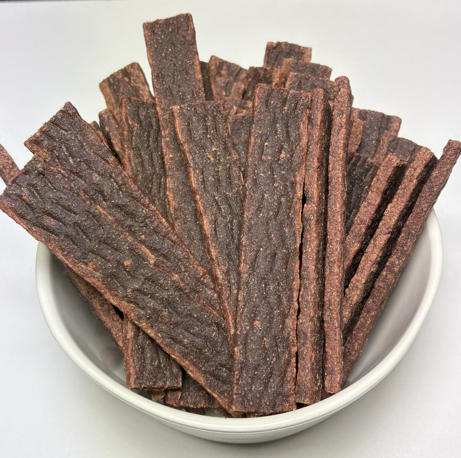 A white bowl filled with a large pile of GoPetPlace kangaroo straps dog treats, viewed from above at a slight angle