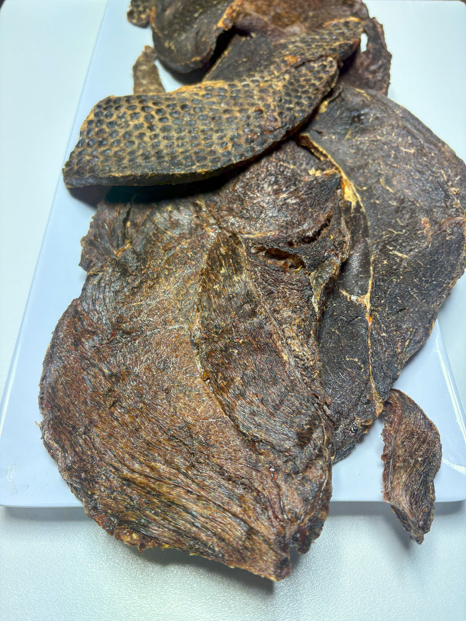 Several large dried topside beef jerky pieces for dogs laid out on a white tray, showing varied natural textures including smooth muscle and dimpled surfaces