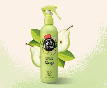 Pet Head Mucky Pup Puppy Spray 300ml in a green trigger-spray bottle, surrounded by illustrated pear and leaf graphics on a light background.