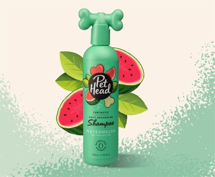 Pet Head Furtastic Knot Detangling Dog Shampoo 300ml green bottle with bone-shaped cap, displayed against a background of fresh watermelon slices and green leaves.