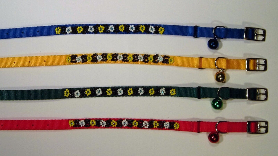 Four beaded cat collars laid flat in blue, yellow, green, and red, each with a floral bead pattern, buckle fastening, and a small matching bell.