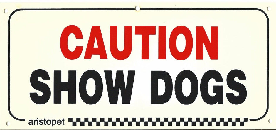 Aristopet Caution Show Dogs acrylic sign with bold red and black text on a cream background, showing pre-drilled hanging holes at each corner.