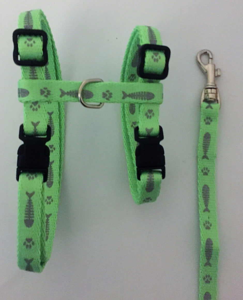 Green adjustable cat harness with fish and paw print pattern, shown laid flat alongside its matching 183 cm lead with metal clip.