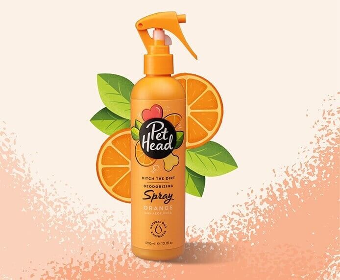 Pet Head Ditch the Dirt Deodorising Dog Spray in an orange trigger-spray bottle, surrounded by orange slices and green leaves on a light peach background