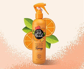 Pet Head Ditch the Dirt Deodorising Dog Spray in an orange trigger-spray bottle, surrounded by orange slices and green leaves on a light peach background